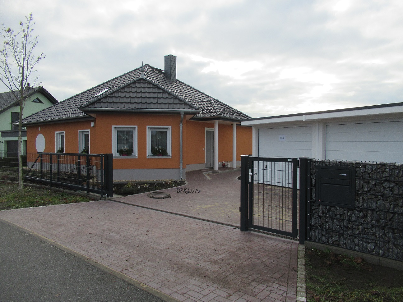 Modernes Einfamilienhaus in Orange mit Garage und Gabionenzaun, gebaut von Berthold - Bau aus Lauta.