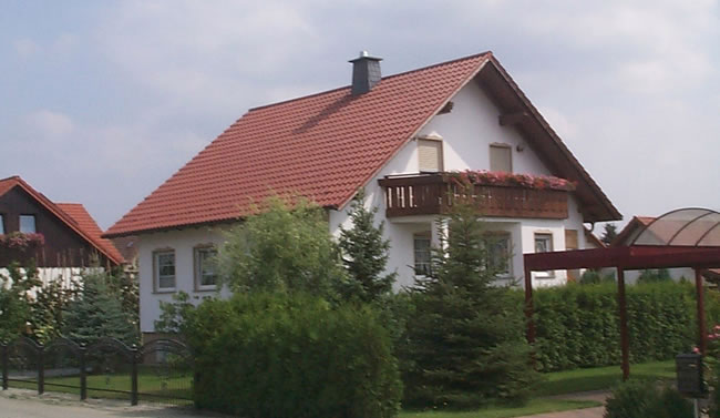 Weißes Einfamilienhaus mit rotem Dach und Balkon, gebaut von Berthold - Bau aus Lauta.