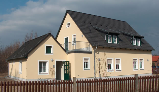 Modernes, hellgelbes Einfamilienhaus mit schwarzem Dach und Balkon, gebaut von Berthold - Bau aus Lauta.