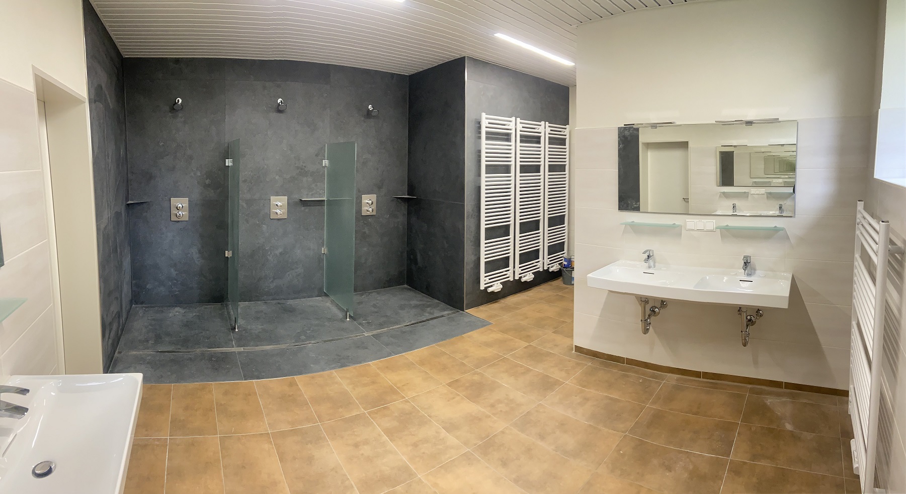 Moderne Duschräume mit mehreren Duschkabinen, Waschtischen und Heizkörpern, gebaut von Berthold-Bau in Lauta.