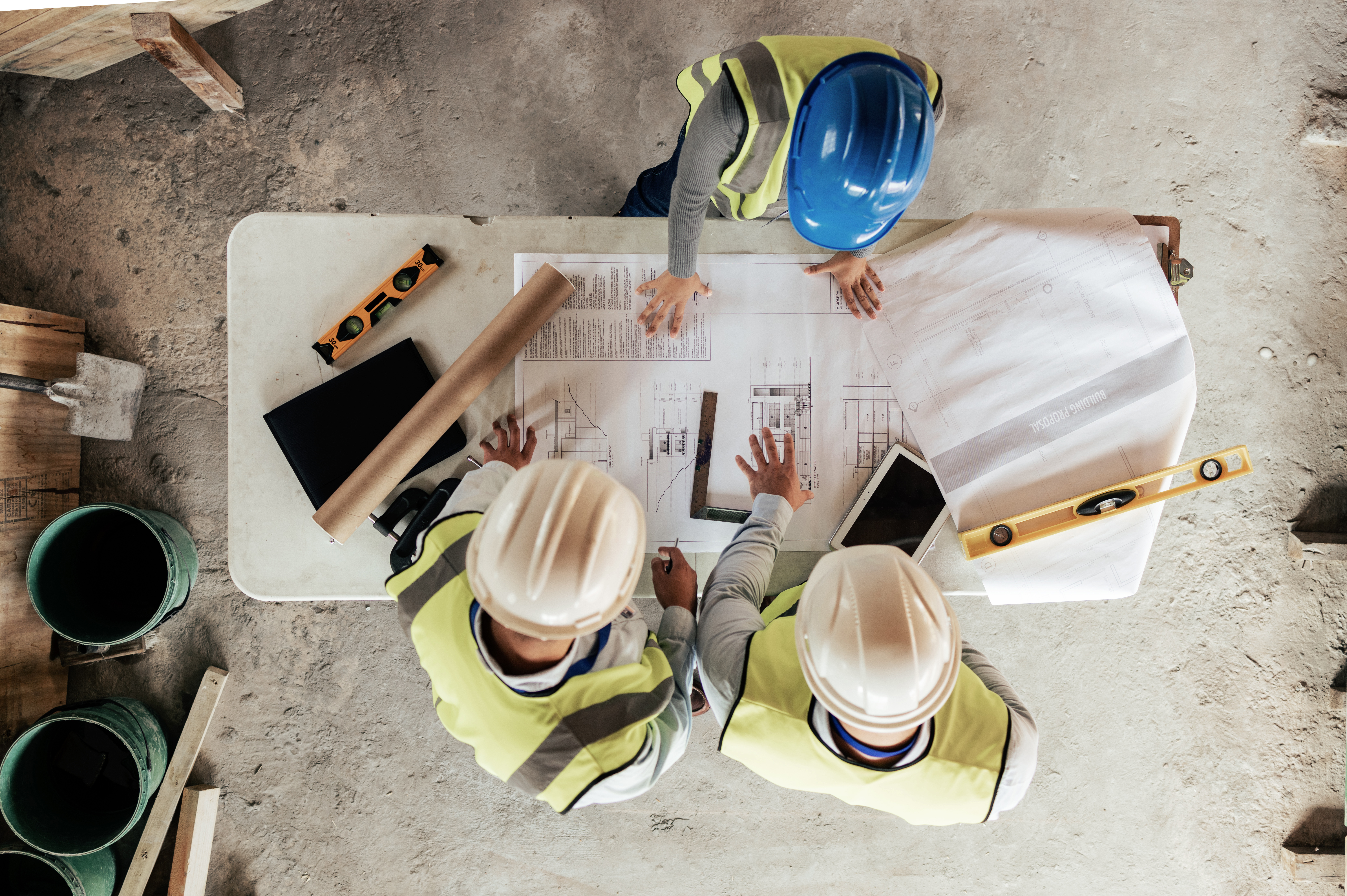 Drei Bauarbeiter in Sicherheitskleidung besprechen Baupläne auf der Baustelle, zeigt Koordination von Berthold-Bau in Lauta.